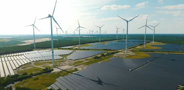 Solarfarm und Windturbinen in der ländlichen Umgebung, umgeben von grünen Feldern und einem klaren blauen Himmel.