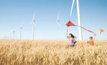 Kinder im Weizenfeld vor Windrädern