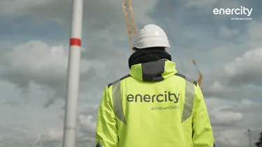 Ein Mann in einer gelben Jacke steht vor einem Windrad.